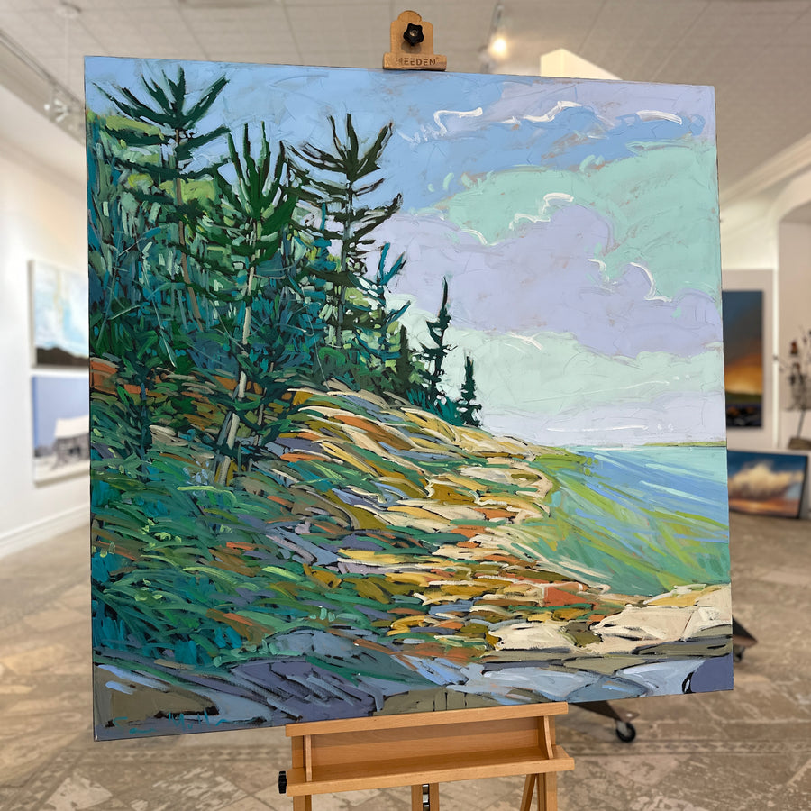 Landscape painting of pines on a rocky shoreline, unframed, on an easel in Butter Gallery