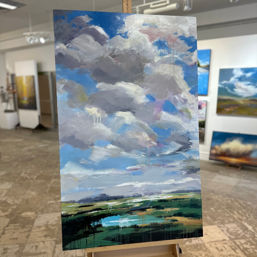 Landscape painting of a cloudy sky over green fields, unframed, on an easel in Butter Gallery
