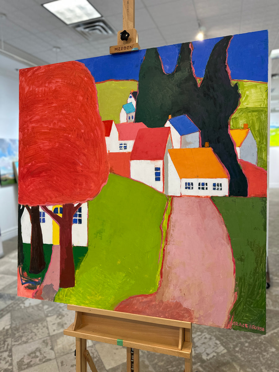 Colourful painting of white houses beside a red tree and a pink path, unframed, on an easel in Butter Gallery